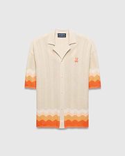 Cream Holden Relaxed Fit Knit Shirt with a wavy knit texture, featuring orange and peach gradient stripes on sleeves and hem, and an embroidered orange Psycho Bunny skull logo on the left chest.