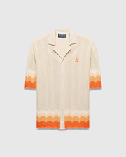 Cream Holden Relaxed Fit Knit Shirt with a wavy knit texture, featuring orange and peach gradient stripes on sleeves and hem, and an embroidered orange Psycho Bunny skull logo on the left chest.