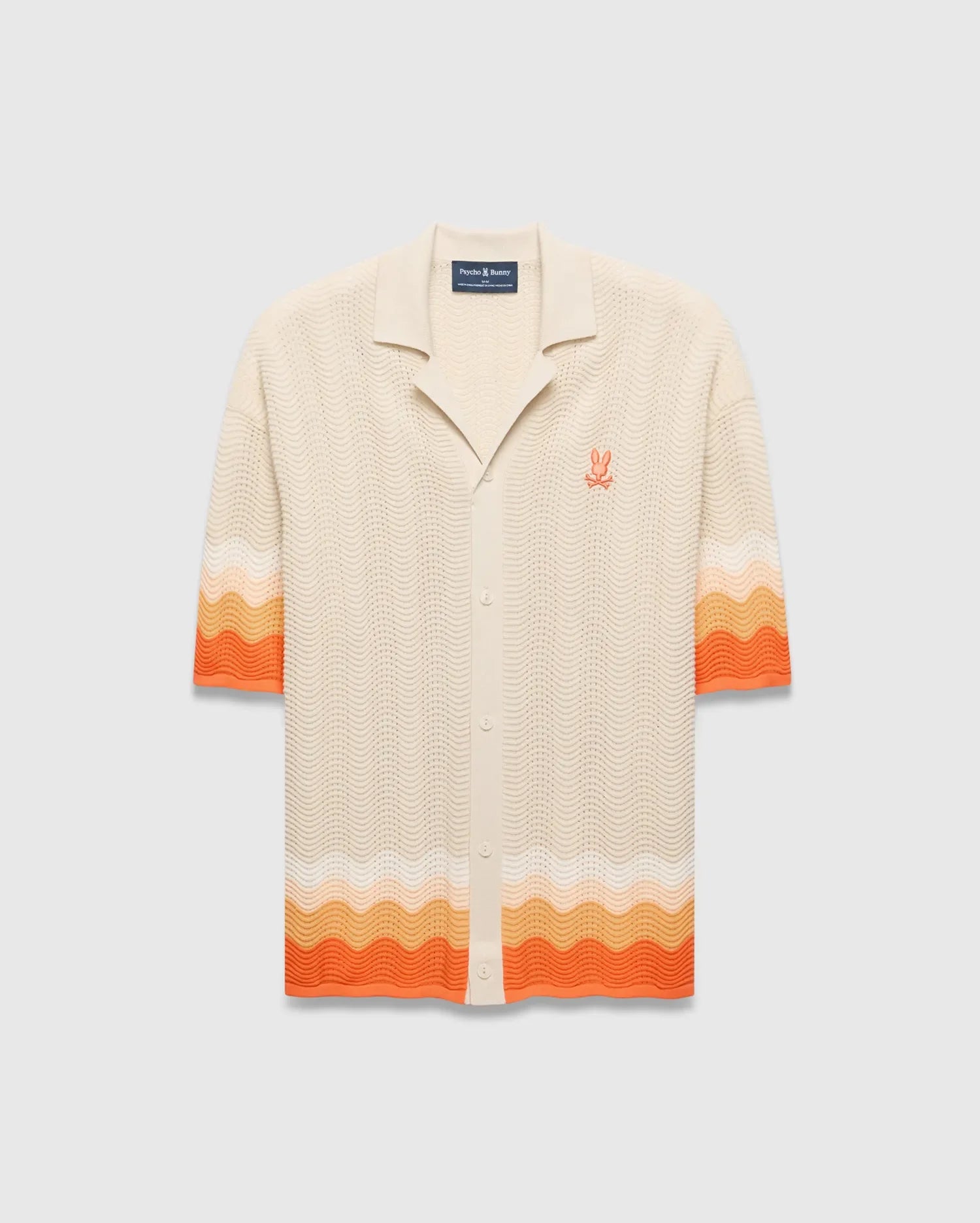 Cream Holden Relaxed Fit Knit Shirt with a wavy knit texture, featuring orange and peach gradient stripes on sleeves and hem, and an embroidered orange Psycho Bunny skull logo on the left chest.