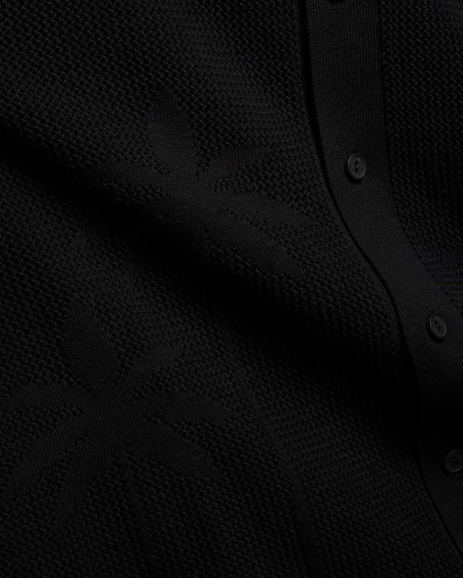 Psycho Bunny Mens Brad Oversized Knit Shirt in deep black, showcasing a unique, intricate textured knit pattern and a refined button placket with matching black buttons.