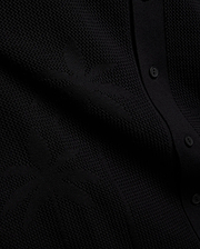 Psycho Bunny Mens Brad Oversized Knit Shirt in deep black, showcasing a unique, intricate textured knit pattern and a refined button placket with matching black buttons.