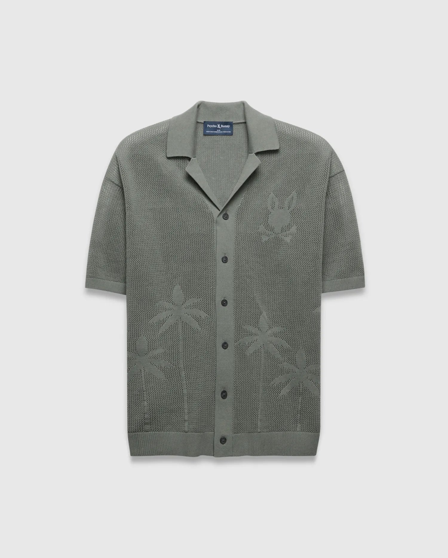 Mens Brad Oversized Knit Shirt in sage green, featuring an open knit texture, a large tonal Psycho Bunny skull logo on the left chest, and subtle palm tree patterns on the lower front.