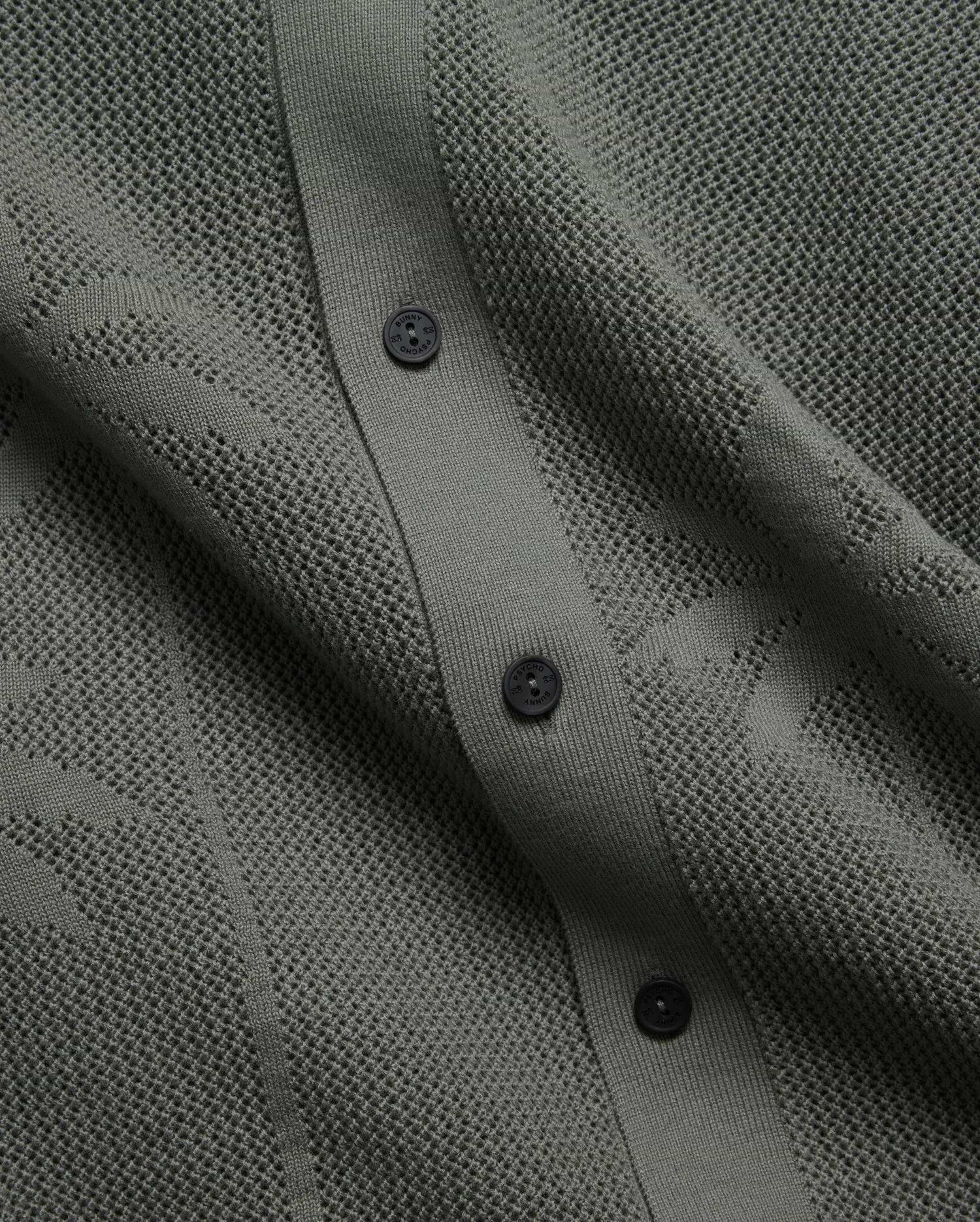 Mens Brad Oversized Knit Shirt in deep sage green, featuring a perforated openwork knit pattern, ribbed button placket, and dark branded Psycho Bunny buttons.