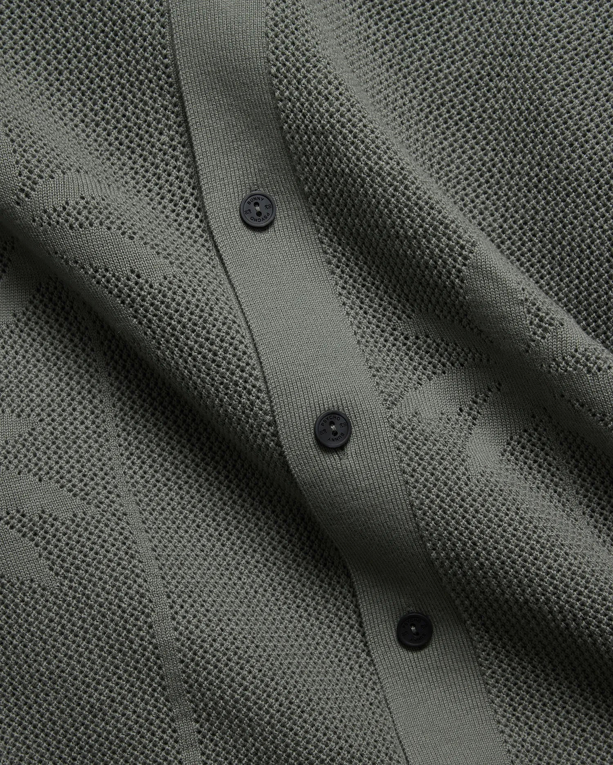 Mens Brad Oversized Knit Shirt in deep sage green, featuring a perforated openwork knit pattern, ribbed button placket, and dark branded Psycho Bunny buttons.