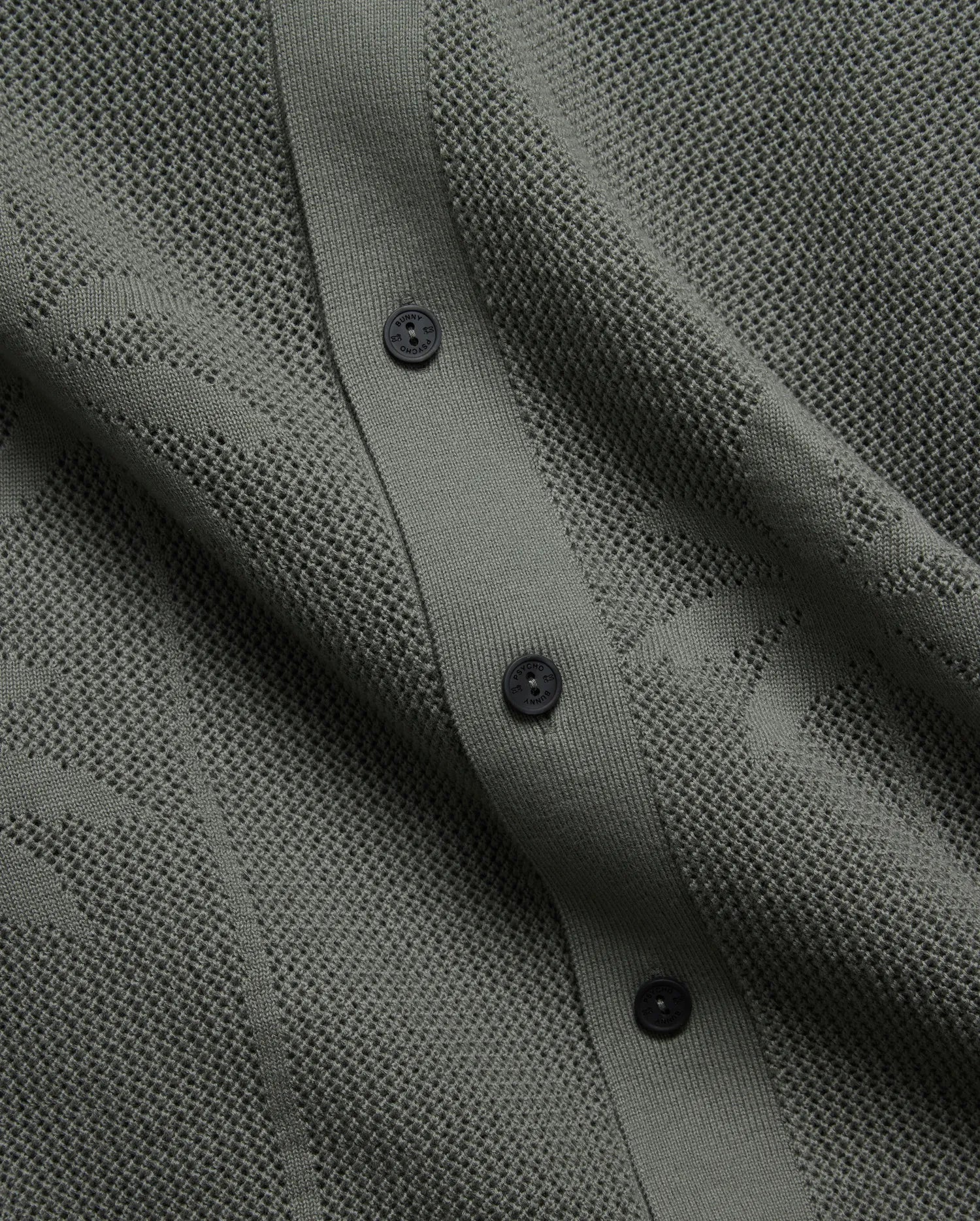 Mens Brad Oversized Knit Shirt in deep sage green, featuring a perforated openwork knit pattern, ribbed button placket, and dark branded Psycho Bunny buttons.
