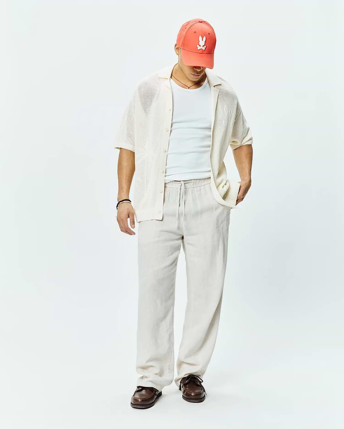 Mens Brad Oversized Knit Shirt in cream, a relaxed short-sleeve open-knit button-up, complemented by a coral Psycho Bunny skull logo baseball cap.