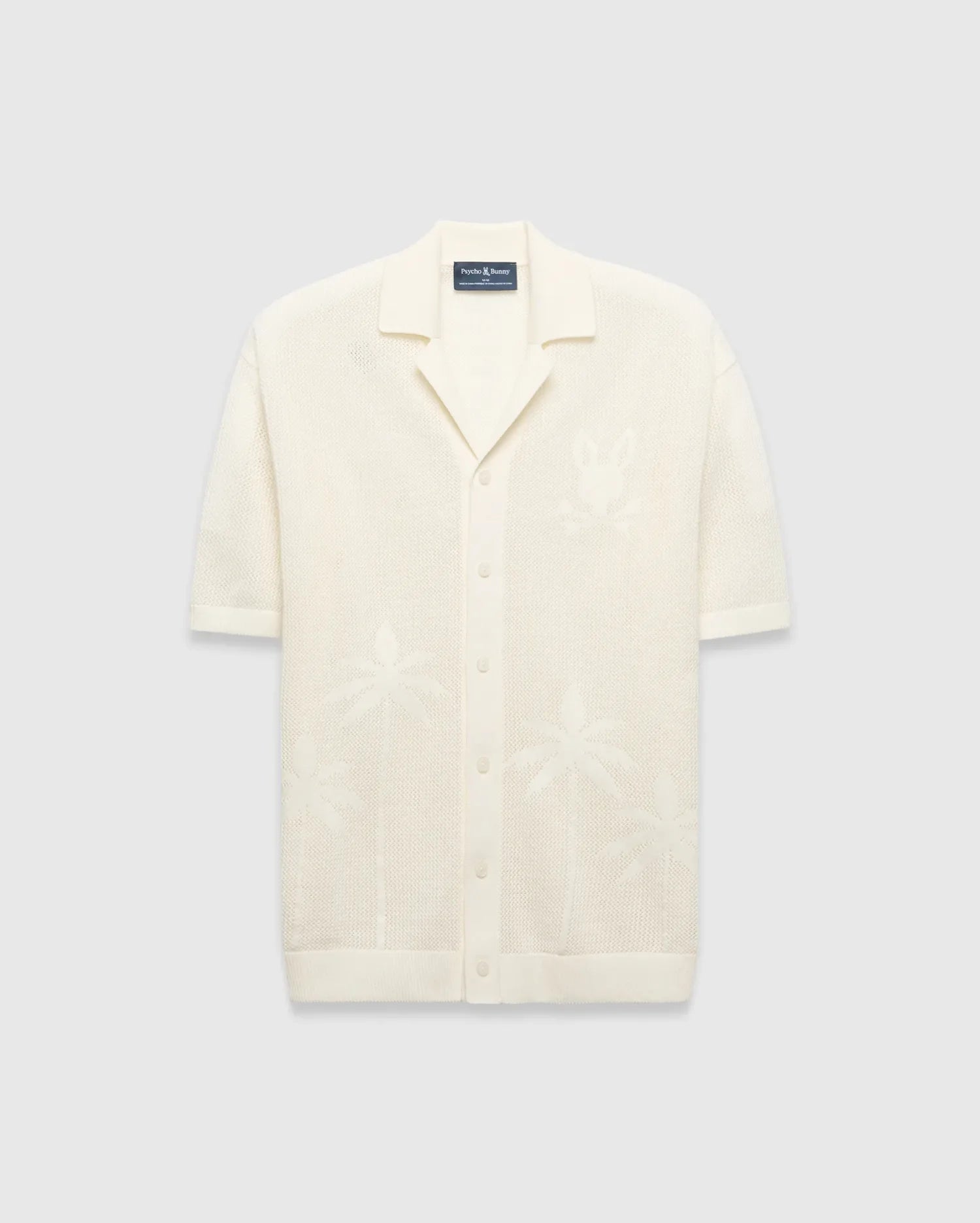 Mens Brad Oversized Knit Shirt in cream, with open-knit texture, subtle jacquard palm tree patterns, large jacquard Psycho Bunny skull logo on left chest, camp collar, and full button placket.