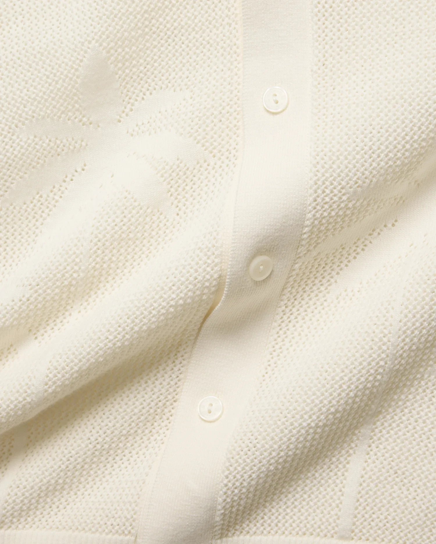 Cream Brad Oversized Knit Shirt with an open-knit texture, featuring a subtle, tone-on-tone Psycho Bunny skull pattern woven throughout and a button-front placket with cream buttons.
