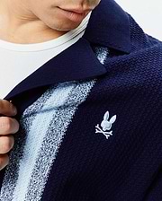 Mens Giles Relaxed Fit Border Knit Shirt in navy blue textured knit, featuring light blue and white vertical stripes, a spread collar, and a small embroidered Psycho Bunny skull logo on the left chest.