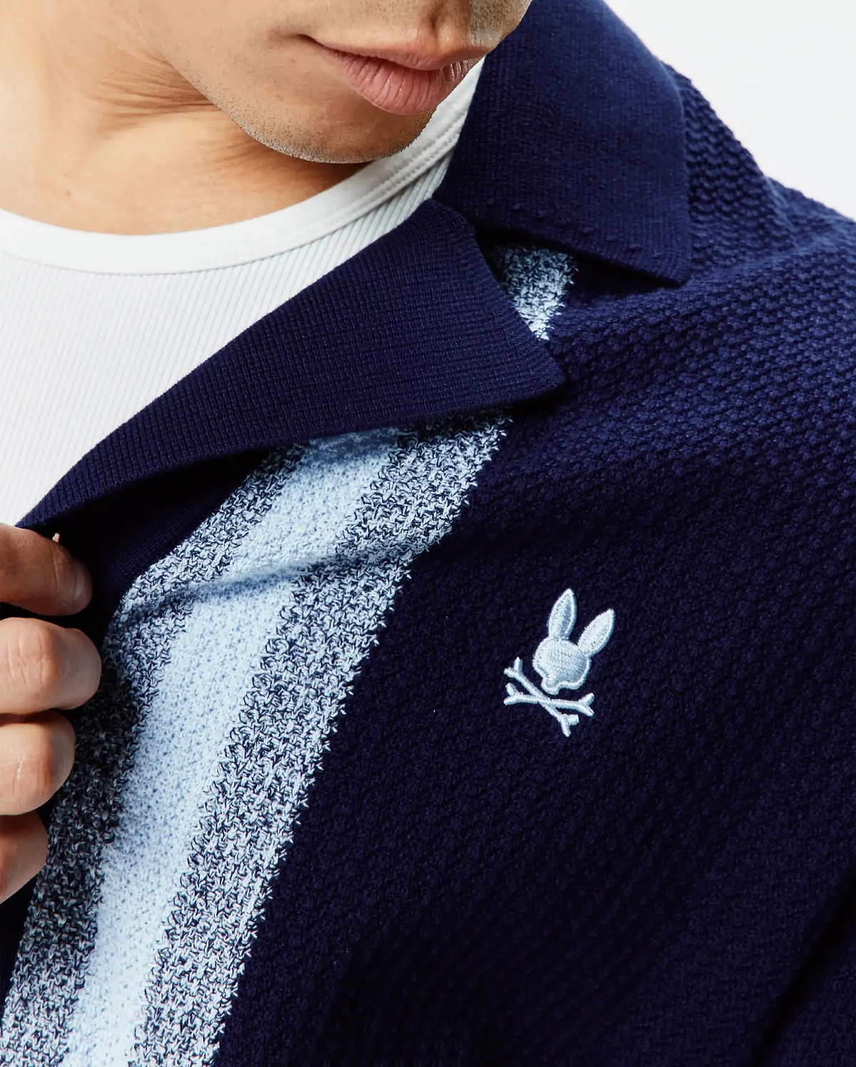 Mens Giles Relaxed Fit Border Knit Shirt in navy blue textured knit, featuring light blue and white vertical stripes, a spread collar, and a small embroidered Psycho Bunny skull logo on the left chest.