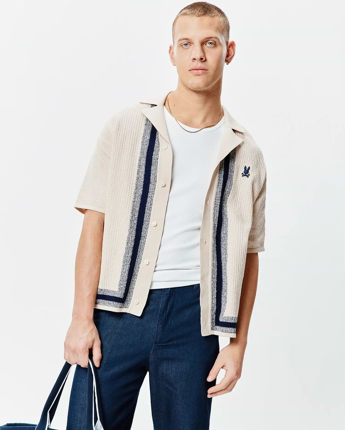 Mens Giles Relaxed Fit Border Knit Shirt, a beige textured knit short-sleeve button-up with navy vertical and border stripes, featuring a small embroidered navy Psycho Bunny skull logo on the left chest.