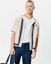 Mens Giles Relaxed Fit Border Knit Shirt, a beige textured knit short-sleeve button-up with navy vertical and border stripes, featuring a small embroidered navy Psycho Bunny skull logo on the left chest.