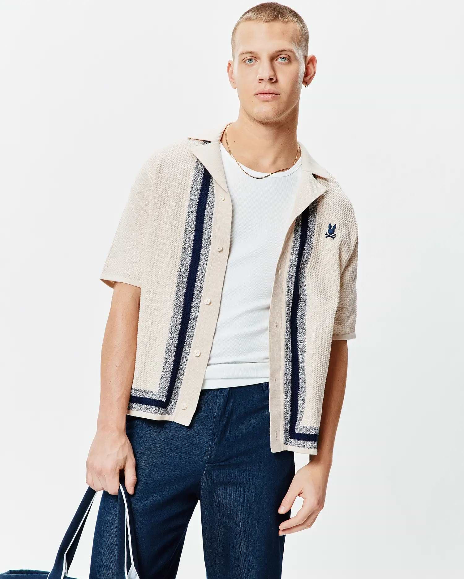 Mens Giles Relaxed Fit Border Knit Shirt, a beige textured knit short-sleeve button-up with navy vertical and border stripes, featuring a small embroidered navy Psycho Bunny skull logo on the left chest.
