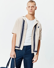 Mens Giles Relaxed Fit Border Knit Shirt, a beige textured knit short-sleeve button-up with navy vertical and border stripes, featuring a small embroidered navy Psycho Bunny skull logo on the left chest.