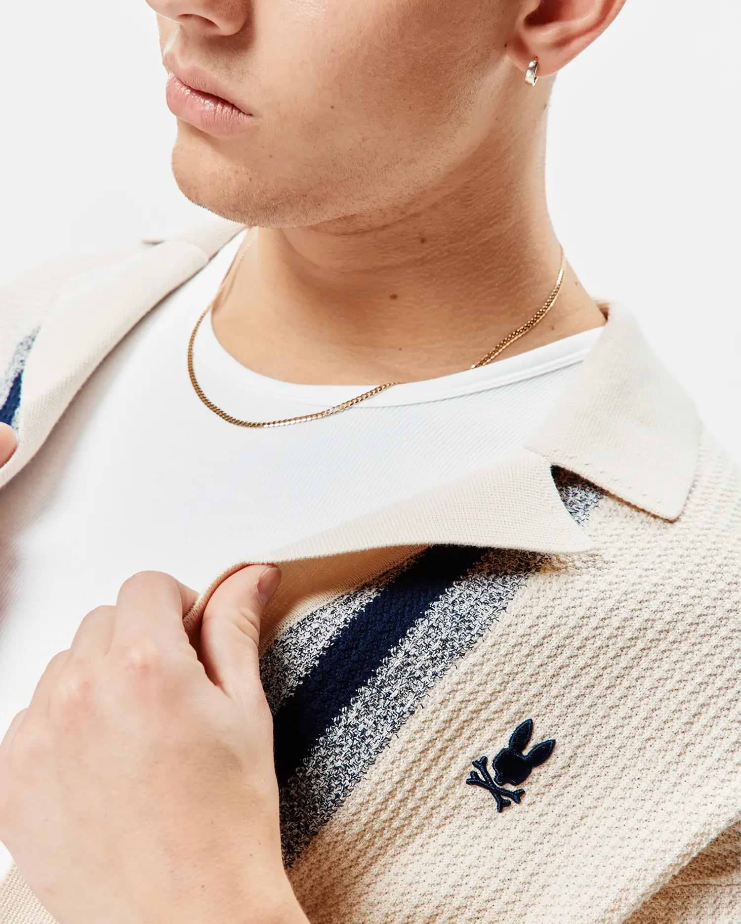 Mens Giles Relaxed Fit Border Knit Shirt in cream textured knit with navy and light blue stripes, featuring a small embroidered navy Psycho Bunny skull logo on the left chest.