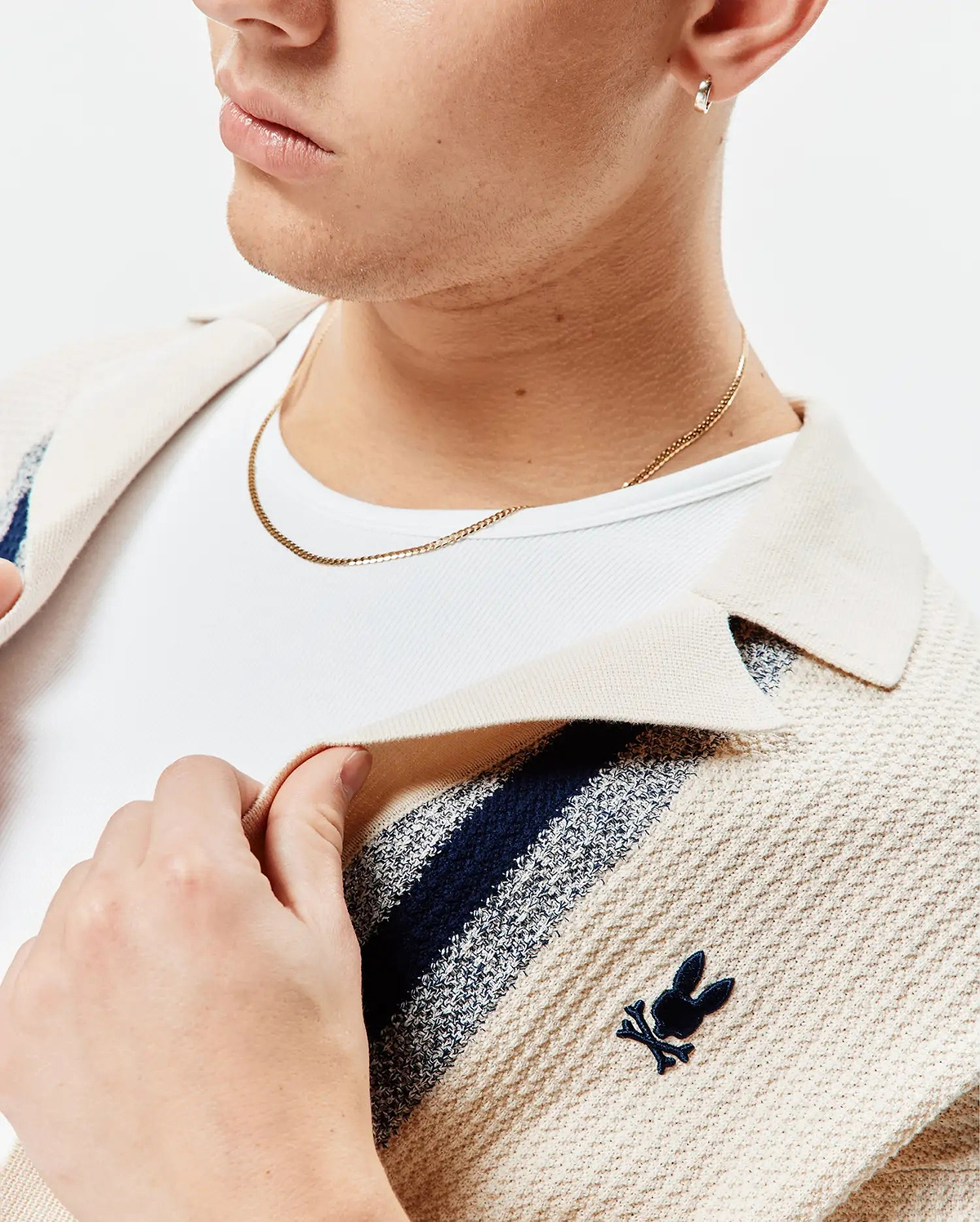 Mens Giles Relaxed Fit Border Knit Shirt in cream textured knit with navy and light blue stripes, featuring a small embroidered navy Psycho Bunny skull logo on the left chest.