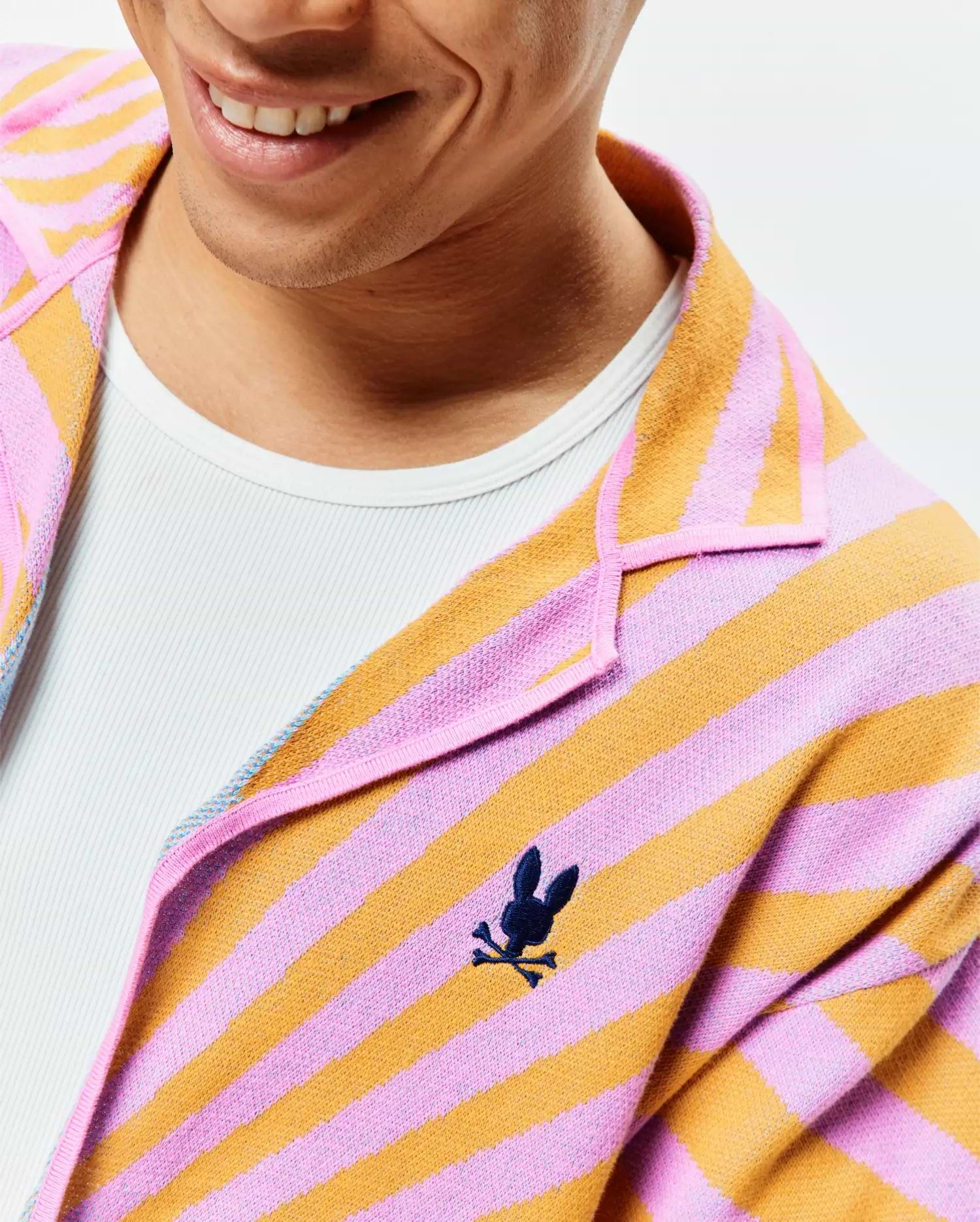 Mens Ray Relaxed Fit Jacquard Shirt, a pink and orange striped jacquard knit with an open collar and a small, dark blue embroidered Psycho Bunny skull logo on the left chest.
