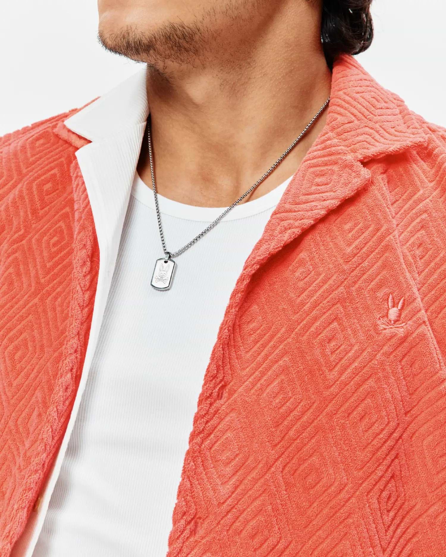 Mens Tristan Shirt in coral terry cloth with an embossed diamond pattern, featuring a small embroidered Psycho Bunny logo on the left chest, worn open over a white ribbed undershirt.