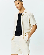 Mens Tristan Shirt: Relaxed fit cream short-sleeve shirt with embossed geometric diamond pattern, textured knit fabric, and small embroidered Psycho Bunny skull logo on left chest, paired with matching shorts.