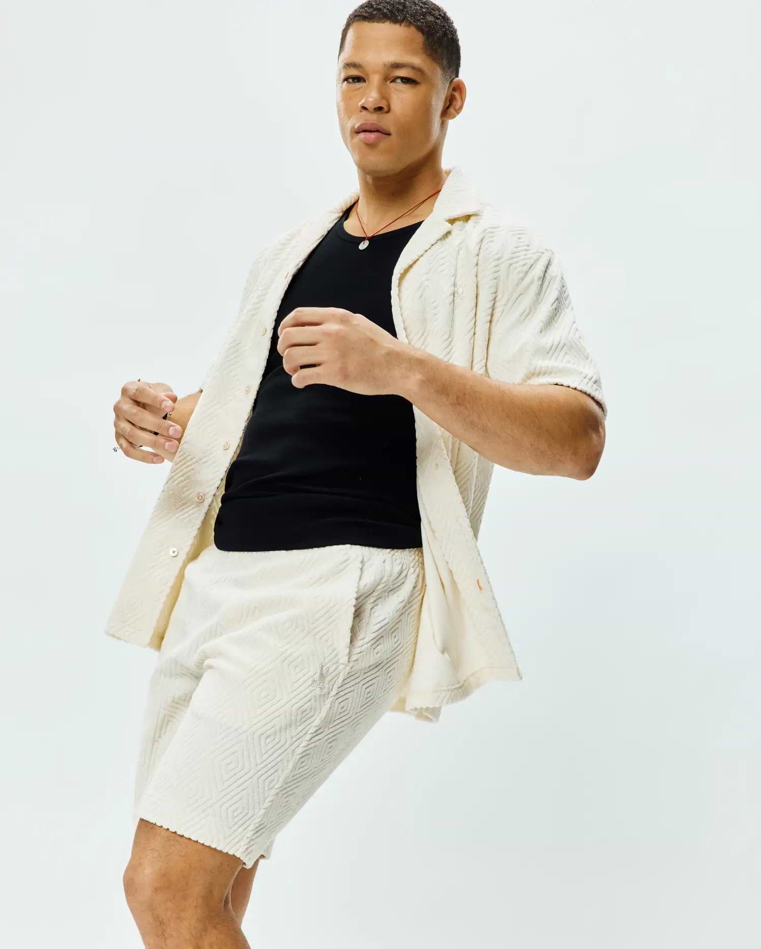 Mens Tristan Shirt: Relaxed fit cream short-sleeve button-up shirt and matching shorts, both featuring a textured geometric diamond pattern and a small embroidered Psycho Bunny skull logo on the shorts.