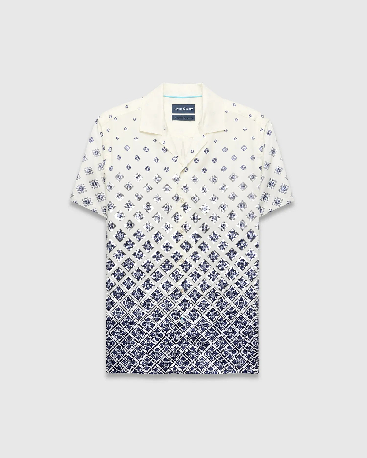Mens Tobias Tencel Shirt, a relaxed fit cream short-sleeve camp collar shirt with a navy blue diamond pattern that intensifies downwards, featuring the iconic Psycho Bunny skull logo.