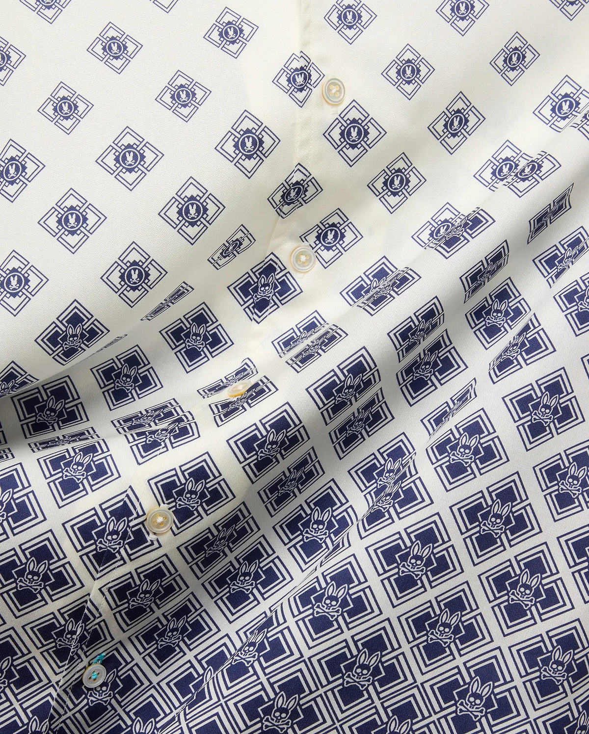 Mens Tobias Tencel Shirt features an off-white smooth Tencel fabric with a repeating navy blue geometric pattern incorporating the iconic Psycho Bunny skull logo throughout, detailed with light buttons.