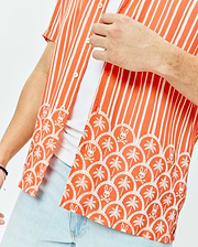 Mens Brad Tencel Shirt, an orange and white striped short-sleeve shirt with a relaxed fit, featuring a lower scalloped pattern of white palm trees and Psycho Bunny skull logos on smooth Tencel fabric.