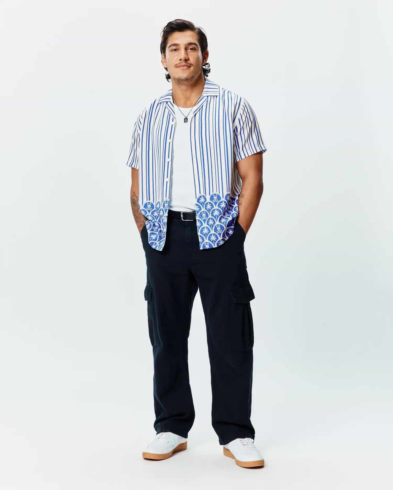 Mens Brad Tencel Shirt: Relaxed fit white short-sleeve button-up with blue vertical stripes and a unique blue and white scalloped pattern featuring small Psycho Bunny skull logos on the hem.