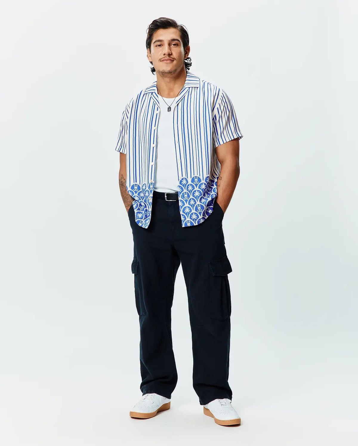 Mens Brad Tencel Shirt: Relaxed fit white short-sleeve button-up with blue vertical stripes and a unique blue and white scalloped pattern featuring small Psycho Bunny skull logos on the hem.