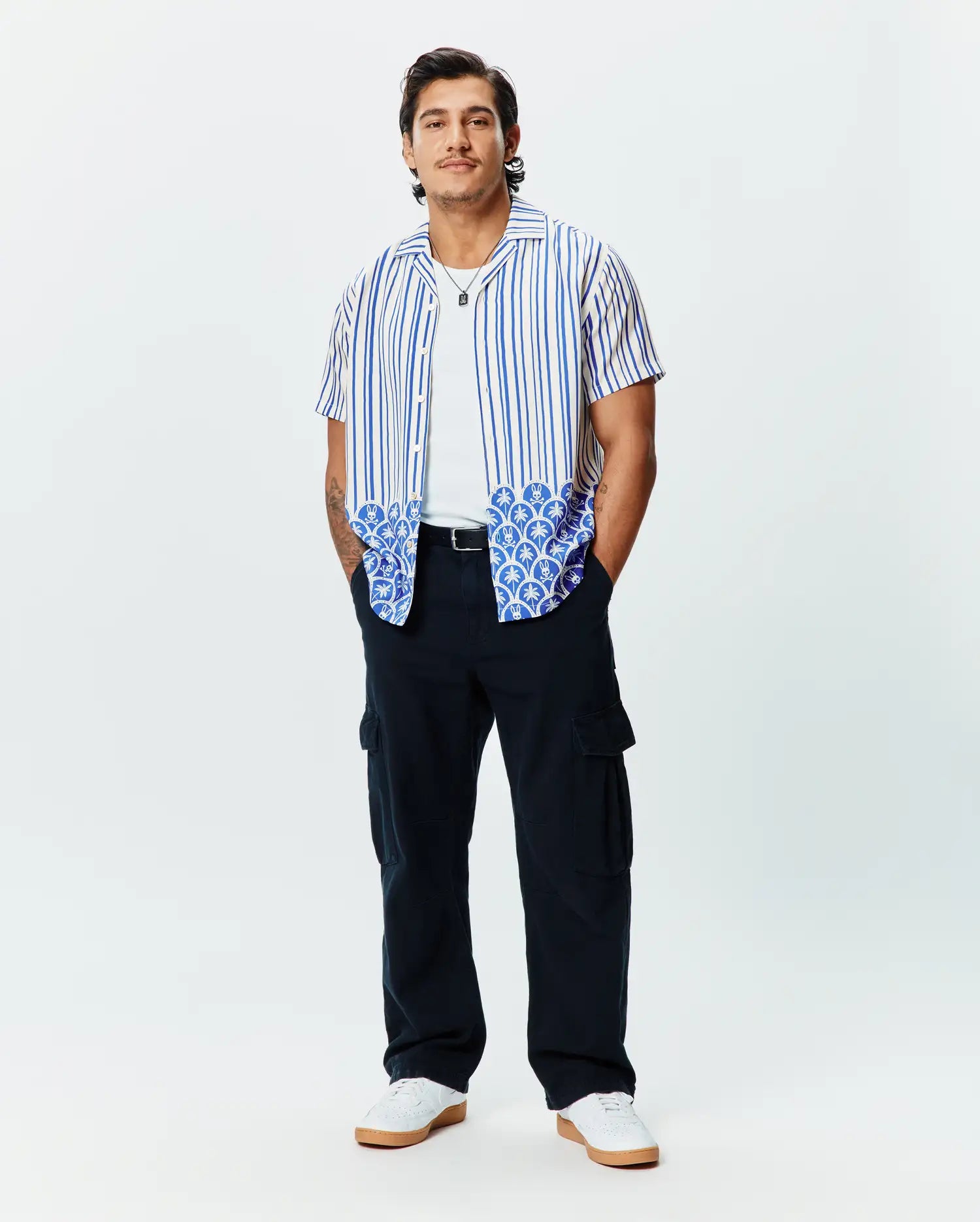 Mens Brad Tencel Shirt: Relaxed fit white short-sleeve button-up with blue vertical stripes and a unique blue and white scalloped pattern featuring small Psycho Bunny skull logos on the hem.