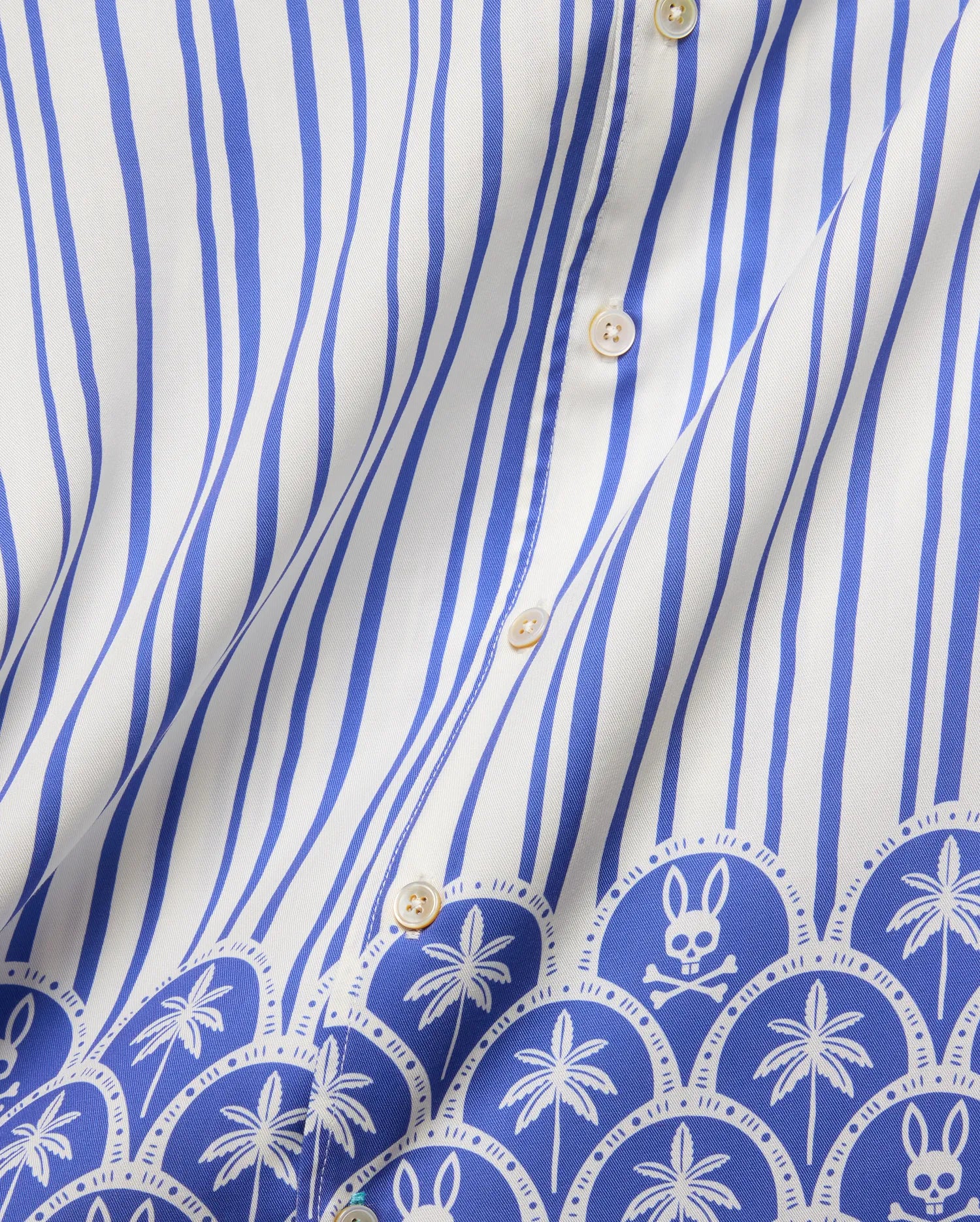 Mens Brad Tencel Shirt featuring a white and royal blue vertical stripe pattern, transitioning to a decorative border with repeating palm trees and the iconic Psycho Bunny skull logo on smooth Tencel fabric.