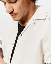 Mens Sunny Linen Shirt, a relaxed fit off-white linen camp collar shirt featuring a small embroidered Psycho Bunny skull logo on the left chest and black and teal chevron sleeve pattern.