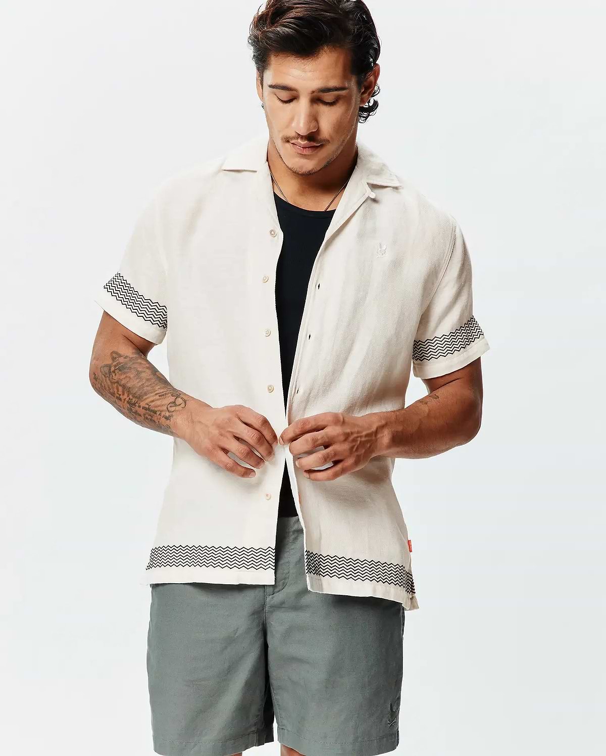 Mens Sunny Linen Shirt, off-white, relaxed fit, with a textured linen fabric, featuring black zigzag patterns on short sleeves and hem, plus a small embroidered Psycho Bunny skull logo on the left chest.