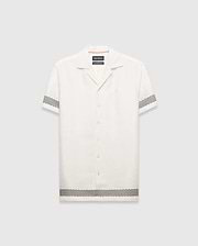 Mens Sunny Linen Shirt, an off-white relaxed linen camp collar shirt, features black zigzag patterns on sleeves and hem, an embroidered Psycho Bunny logo left chest, and orange collar trim.