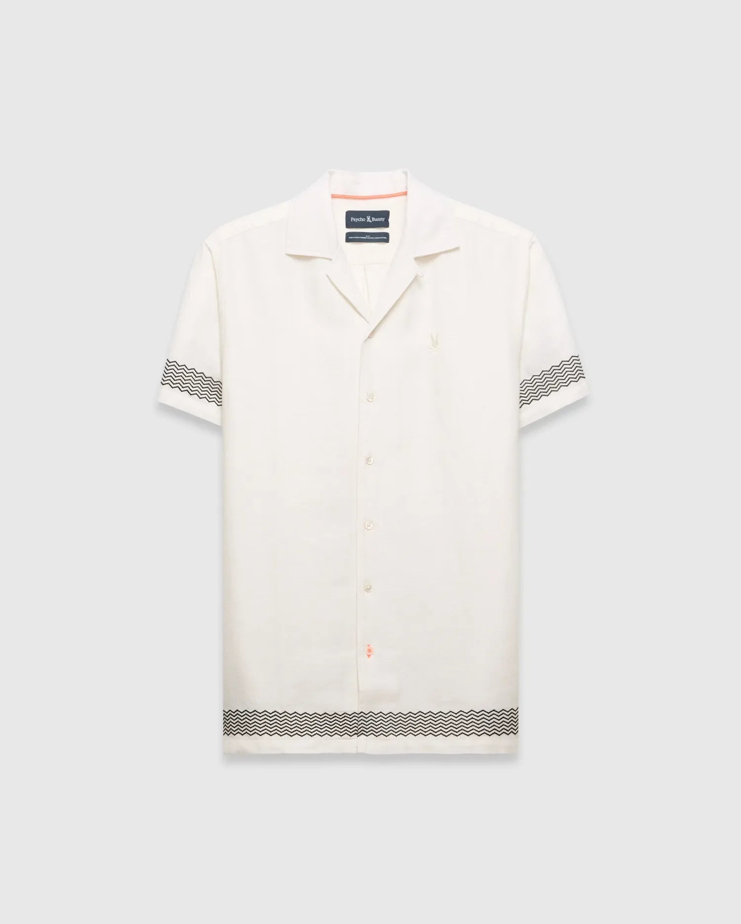 Mens Sunny Linen Shirt, an off-white relaxed linen camp collar shirt, features black zigzag patterns on sleeves and hem, an embroidered Psycho Bunny logo left chest, and orange collar trim.