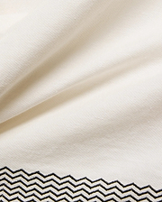Mens Sunny Linen Shirt in crisp cream linen fabric, showcasing a refined black embroidered zigzag pattern with intricate stitching detail along the bottom hem.