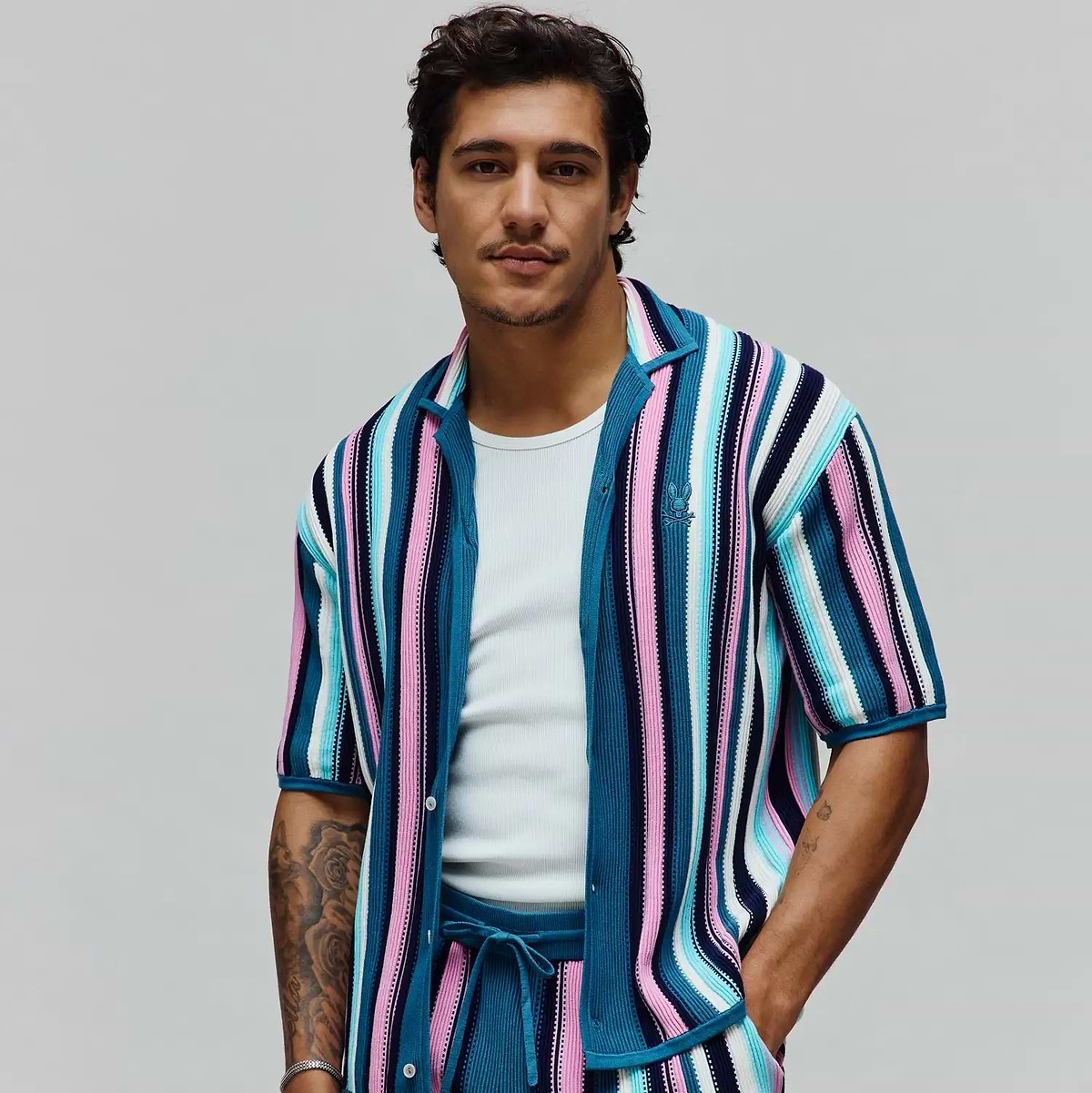 Mens Cliff Shirt, a relaxed fit, short-sleeve knit shirt featuring bold vertical stripes in teal, pink, white, and navy. Small embroidered Psycho Bunny skull logo on the left chest.
