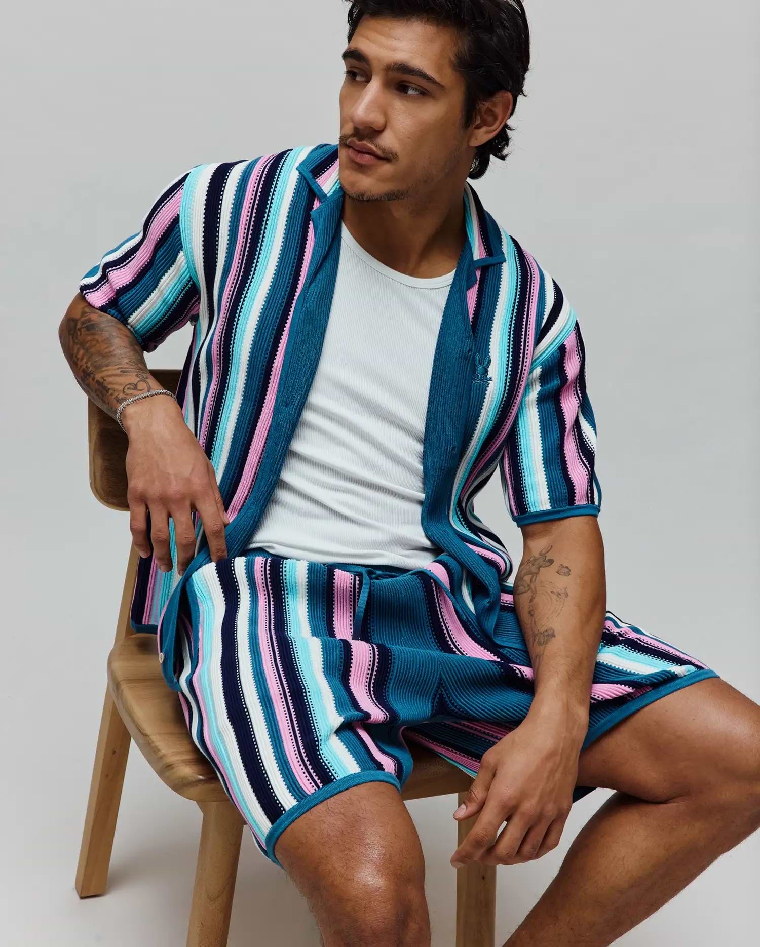 MENS CLIFF SHIRT, a relaxed fit, ribbed knit short-sleeve shirt with bold vertical stripes in teal, pink, light blue, white, and navy, featuring a small embroidered Psycho Bunny skull logo on the chest.