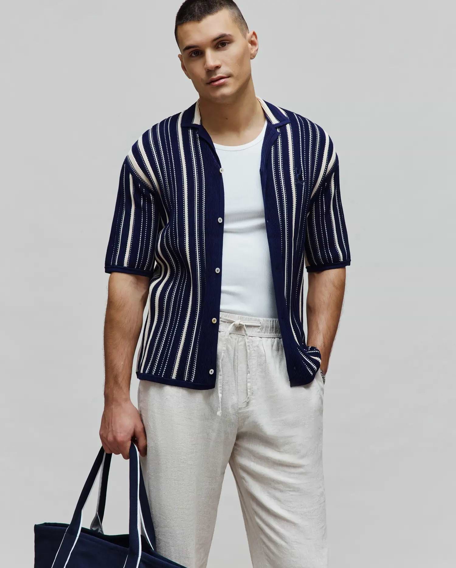 Mens Cliff Shirt, a navy blue knitted short-sleeve button-up shirt with white vertical stripes, an open collar, and a small embroidered Psycho Bunny skull logo on the left chest.