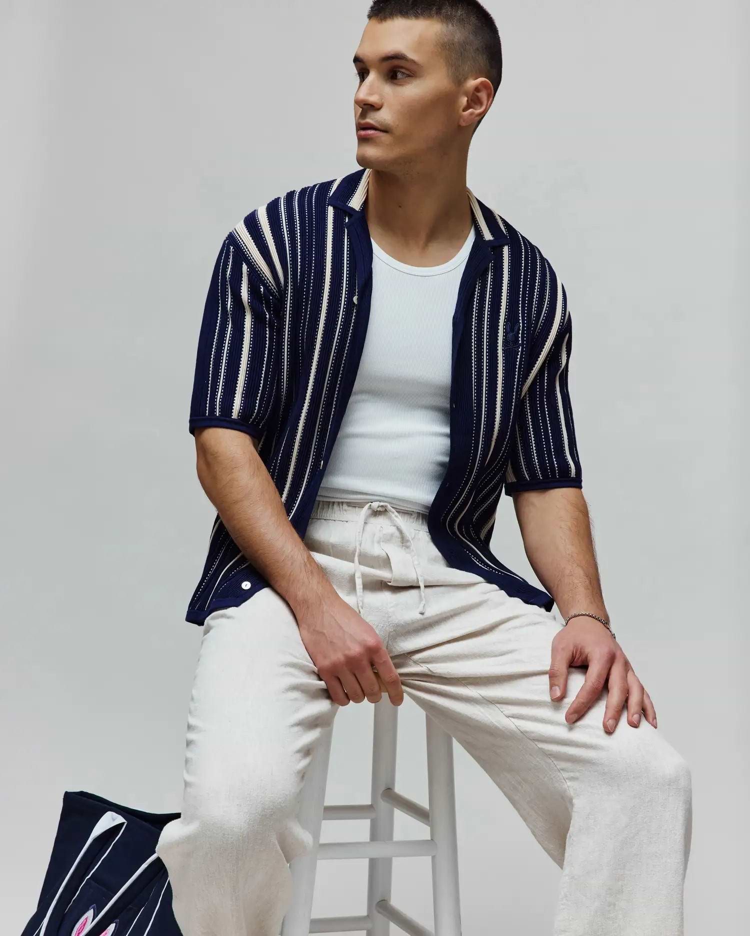 Mens Cliff Shirt: Navy blue textured knit short-sleeve shirt with varied cream vertical stripes, a relaxed fit, and a small embroidered Psycho Bunny skull logo on the left sleeve.