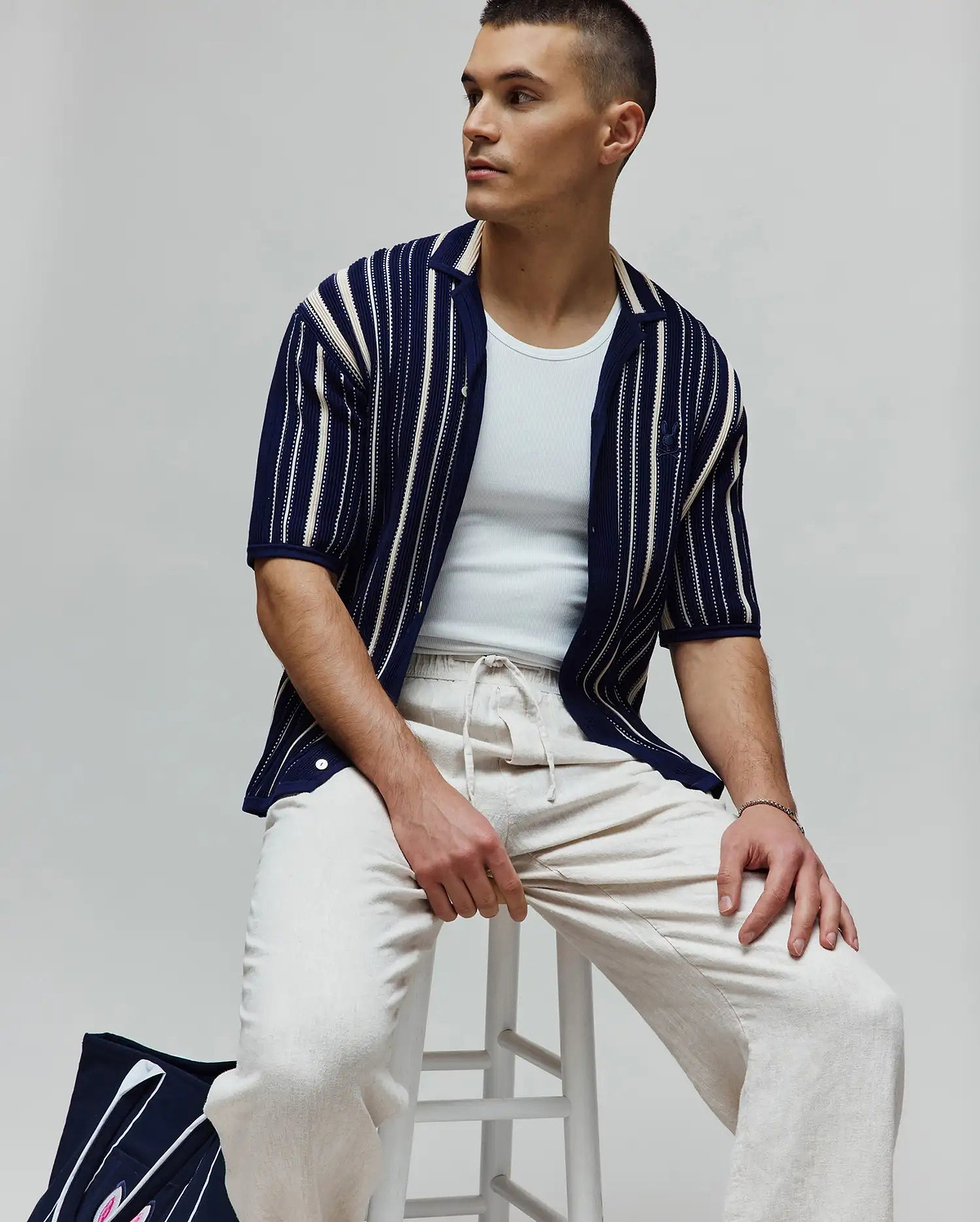 Mens Cliff Shirt: Navy blue textured knit short-sleeve shirt with varied cream vertical stripes, a relaxed fit, and a small embroidered Psycho Bunny skull logo on the left sleeve.