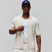 Mens Cliff Shirt, a relaxed fit cream and light beige striped pleated knit short-sleeve button-up shirt with a small embroidered Psycho Bunny skull logo on the left chest.