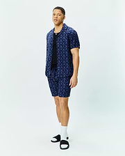 Mens Brad All Over Print Linen Blend Shirt and matching shorts in navy blue, featuring a relaxed fit, camp collar, and an intricate all-over pattern of light blue Psycho Bunny skull logos and palm trees.