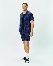 Mens Brad All Over Print Linen Blend Shirt and matching shorts in navy blue, featuring a relaxed fit, camp collar, and an intricate all-over pattern of light blue Psycho Bunny skull logos and palm trees.