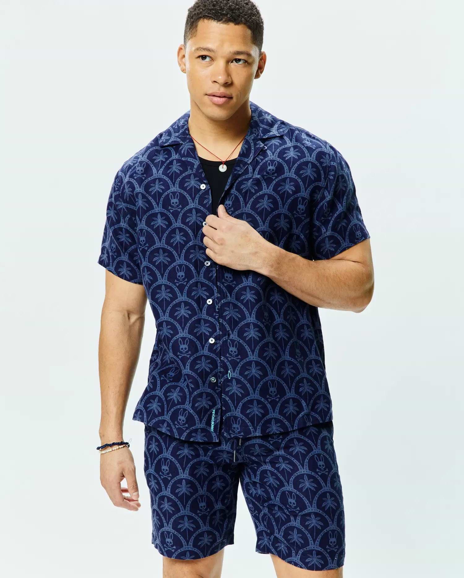 Mens Brad All Over Print Linen Blend Shirt in navy with a light blue all-over scalloped pattern featuring palm trees and small Psycho Bunny skull logos, a relaxed fit, and a camp collar.