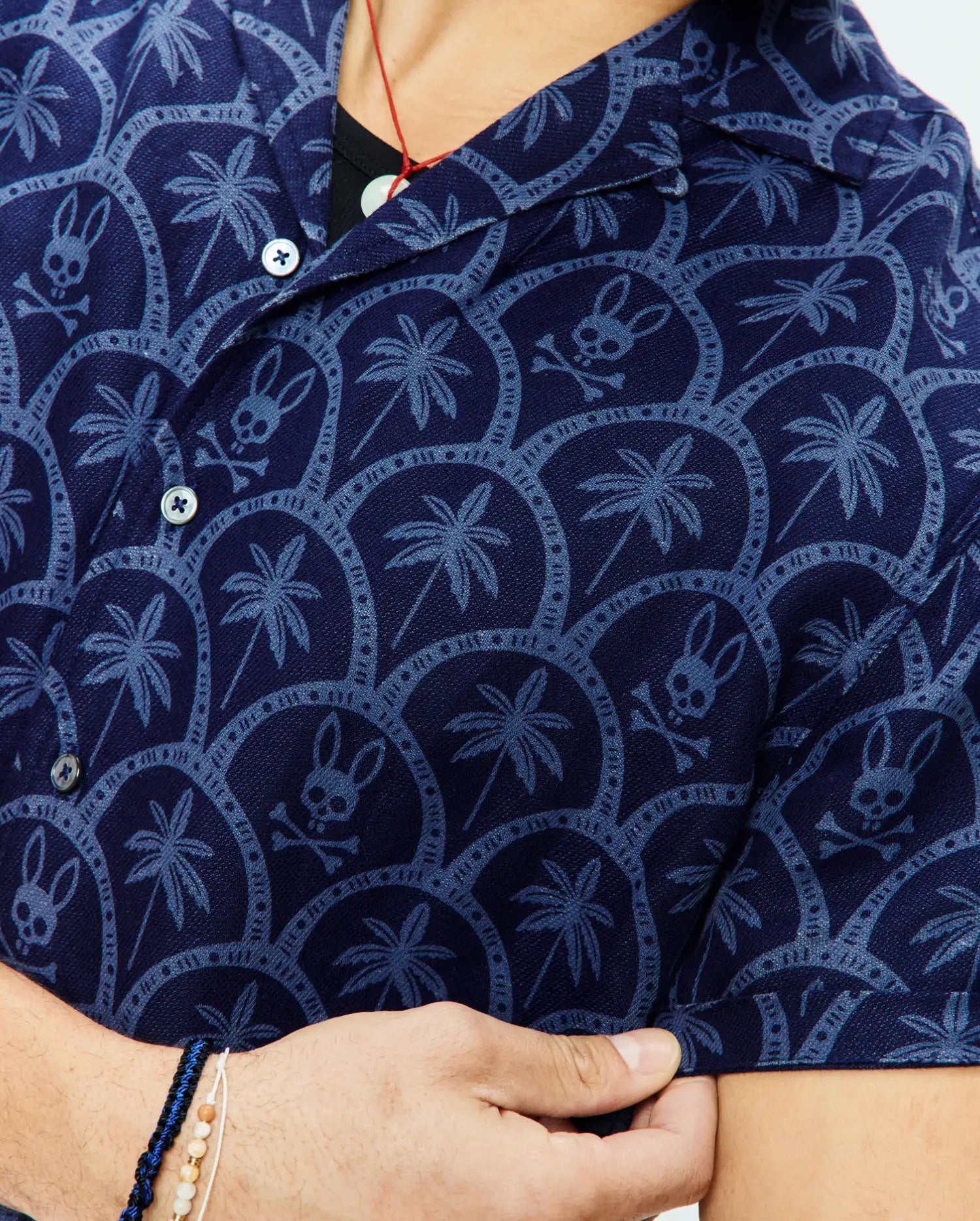 Mens Brad All Over Print Linen Blend Shirt in navy blue, featuring a lighter blue all-over pattern of palm trees, Psycho Bunny skull logos, and intricate circular designs on a textured linen blend fabric.