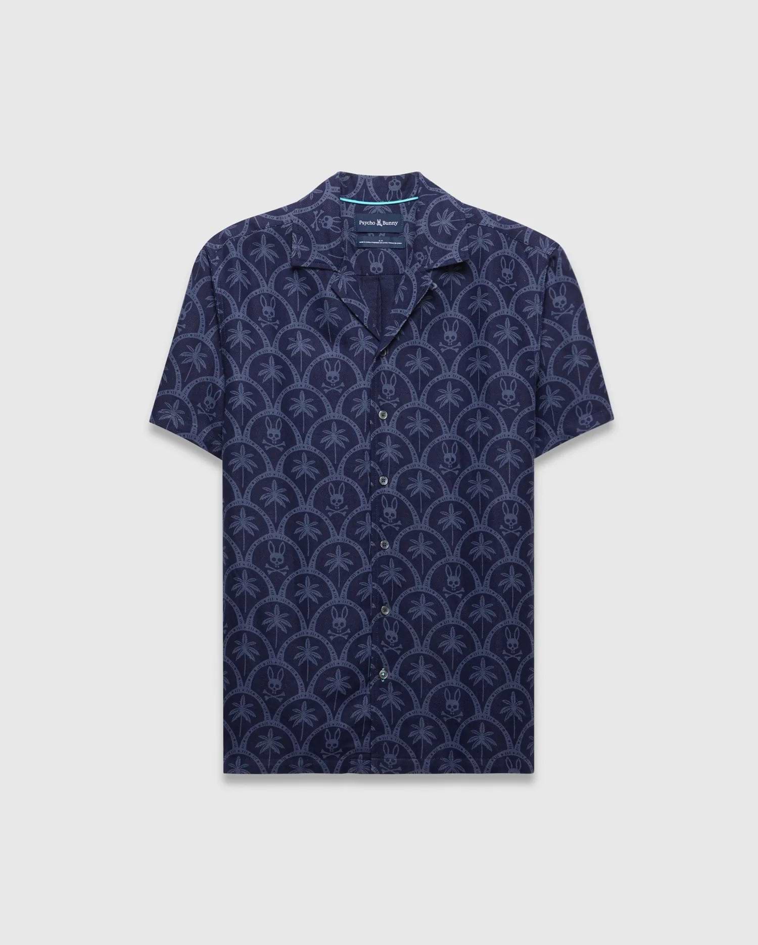 Mens Brad All Over Print Linen Blend Shirt in dark navy with a light blue repeating pattern of palm trees and small Psycho Bunny skull logos, featuring a relaxed fit and camp collar.