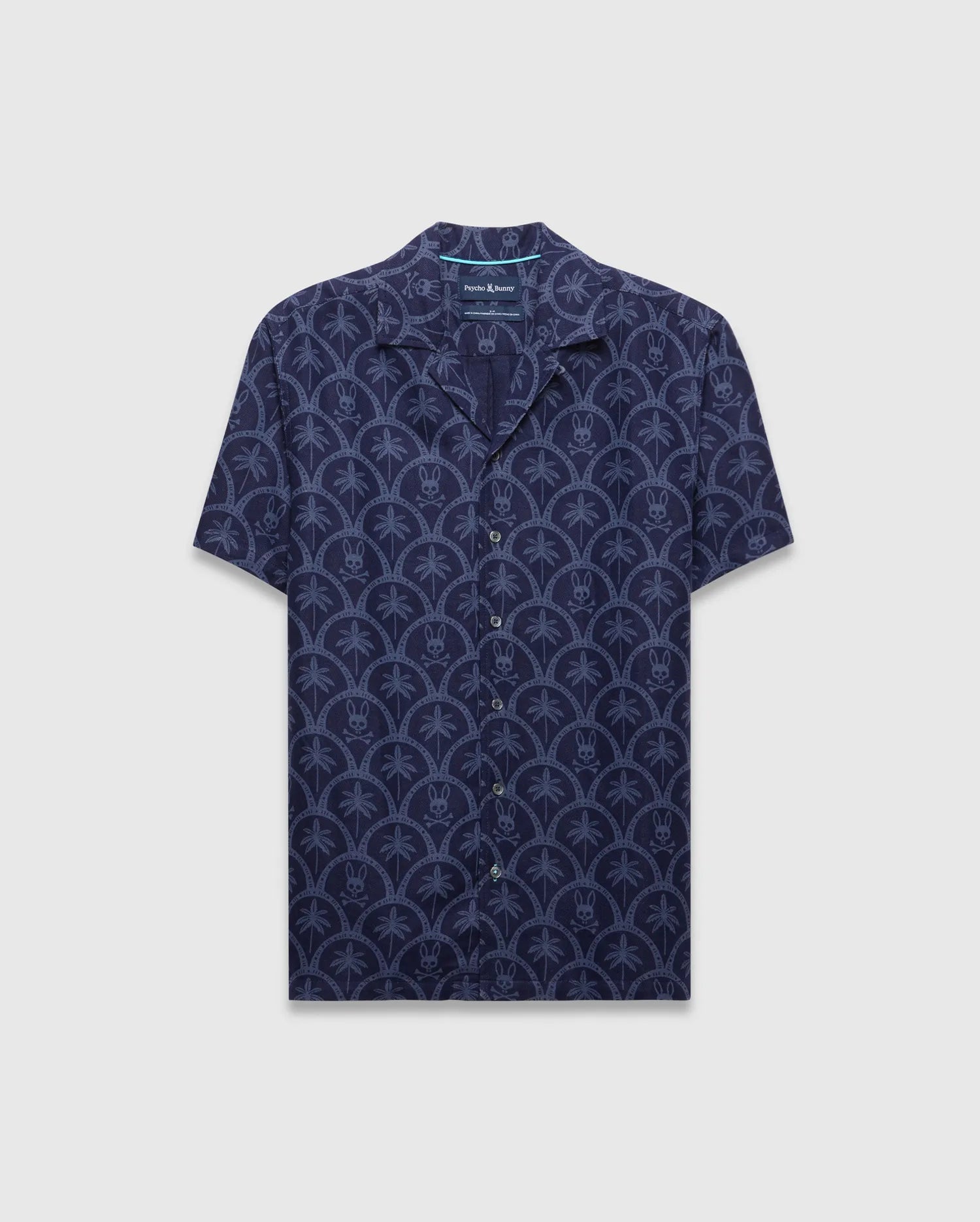 Mens Brad All Over Print Linen Blend Shirt in dark navy with a light blue repeating pattern of palm trees and small Psycho Bunny skull logos, featuring a relaxed fit and camp collar.