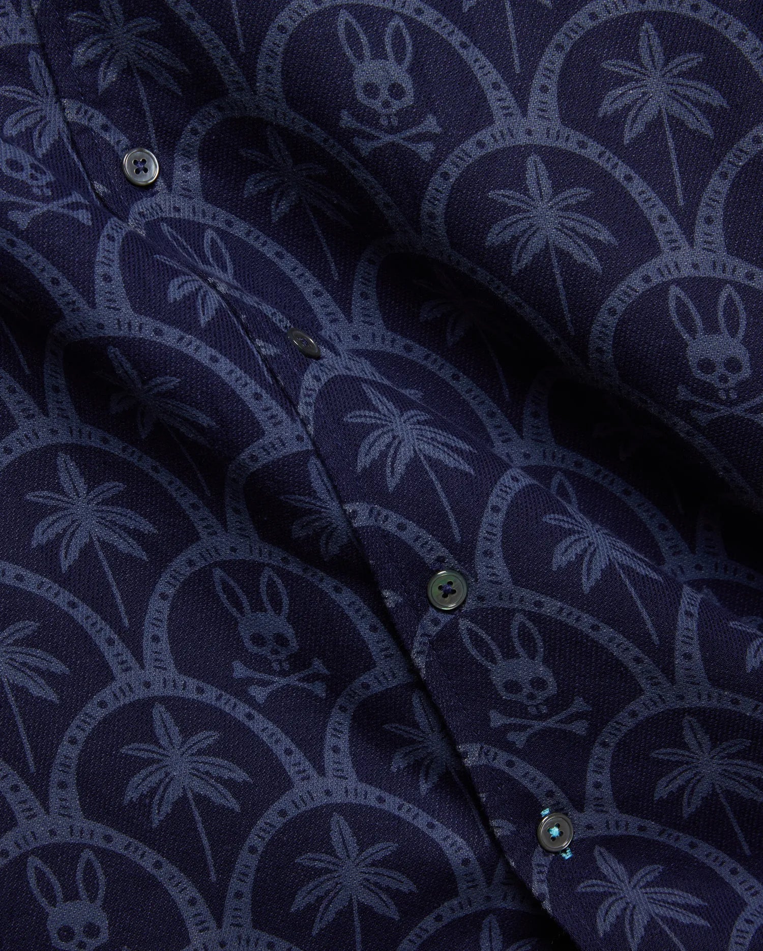 Mens Brad All Over Print Linen Blend Shirt in deep navy, featuring a lighter blue repeating pattern of palm trees and Psycho Bunny skull logos within elegant scalloped arches.