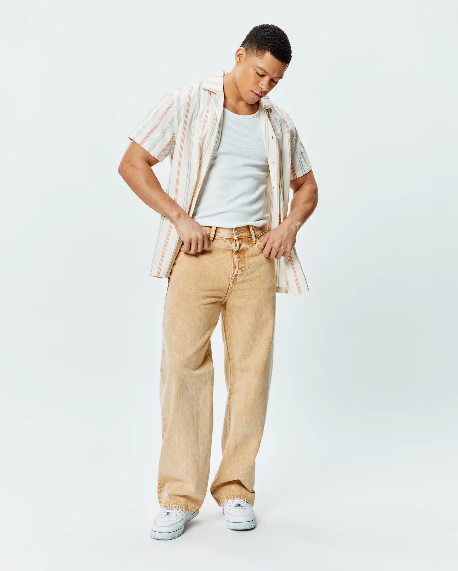 Mens Antoine Shirt, a relaxed cream short-sleeve button-up with thin red and blue vertical stripes, paired with a white ribbed tank and relaxed washed tan wide-leg denim jeans.
